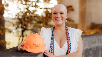 Woman stands at Virginia Tech Pylons with an orange hardhat.