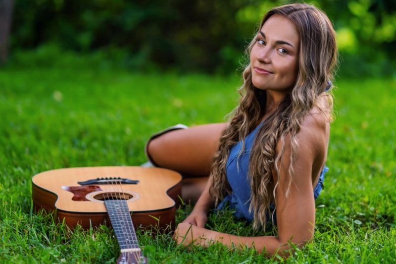 Annalyse Hasty lounges in the grass next to an accousitc guitar.