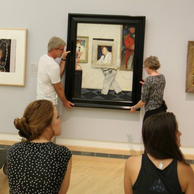 Two people hanging a painting while two people watch